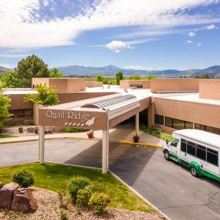 A hospital entrance with a bus parked in front, surrounded by mountains and a clear sky.