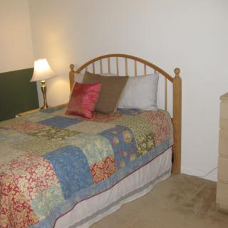 A cozy bedroom with a wooden bed frame, colorful quilt, and bedside lamp.