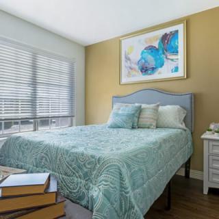 A cozy bedroom with a neatly made bed, showcasing soft natural light from the window and a piece of abstract artwork on the wall.