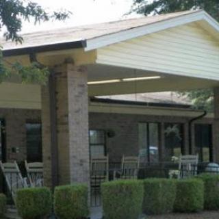 A cozy outdoor seating area under a roof, surrounded by neatly trimmed bushes.