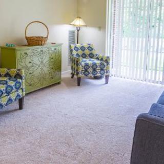 A cozy living room with patterned chairs, a green cabinet, and a floor lamp near a large window.