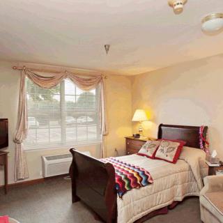 A cozy bedroom with wooden furniture, featuring a bed, lamp, TV, and a window with curtains.