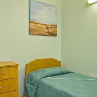 A minimalist bedroom with a single bed, a wooden dresser, and a landscape painting on the wall.