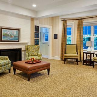 A cozy living room featuring comfortable chairs, a wooden coffee table, and a fireplace, adorned with elegant curtains and a painting on the wall.
