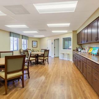 A spacious and well-lit dining area featuring wooden floors, tables, chairs, and cabinetry.