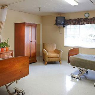 A hospital room featuring beds, a chair, and a television.