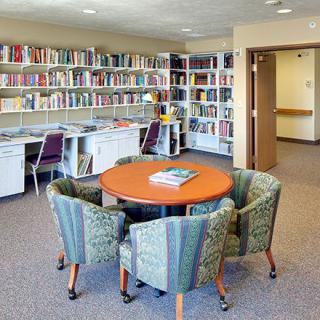 A cozy library reading room with bookshelves and a round table surrounded by chairs.