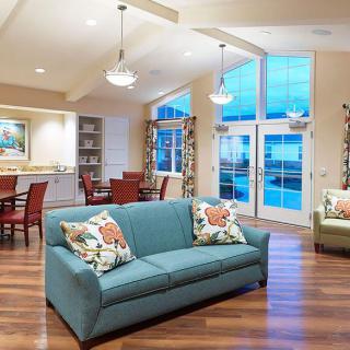 A modern open-concept living and dining area featuring a blue sofa, wood flooring, and large windows allowing natural light.