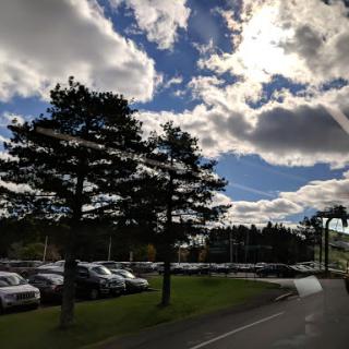 A serene view of the sky with clouds and trees alongside a parking lot.