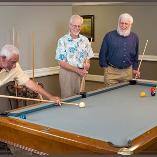 Three elderly men playing a game of billiards indoors.