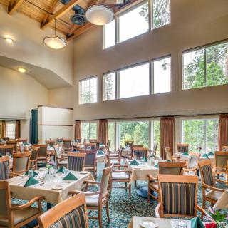 A spacious restaurant interior featuring a high wooden ceiling and large windows, with neatly arranged tables and chairs.