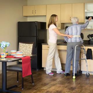 A caregiver assists an elderly person in the kitchen.