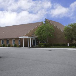 A church building with a sloped roof and a parking lot in the foreground.