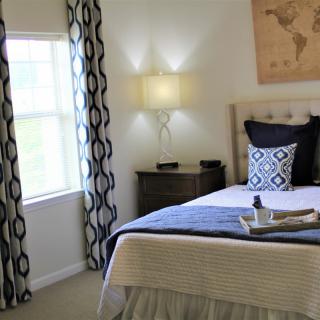 A cozy and stylishly decorated bedroom with a bed, bedside table, lamp, and window with patterned curtains.