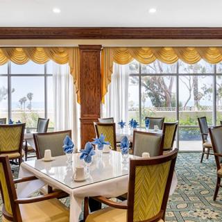 A beautifully arranged restaurant dining area with tables set for guests, featuring large windows and elegant curtains.