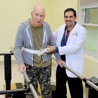 A therapist assists a patient with physical rehabilitation using parallel bars.