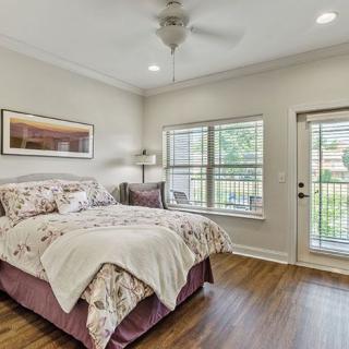 A cozy bedroom featuring a neatly made bed, ceiling fan, and large windows providing natural light.