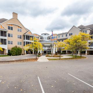 A multi-story residential building with balconies, surrounded by trees and featuring a spacious parking lot.