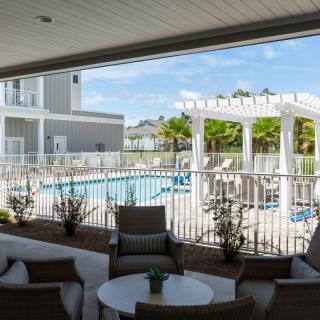 A view of a pool area with lounge chairs and a pergola, seen from an outdoor seating area.