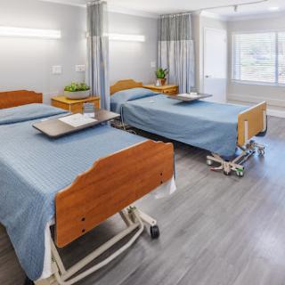 A spacious and well-lit hospital patient room featuring two beds, designed for comfort and recovery.
