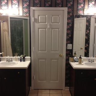 A symmetrical bathroom setup with two sinks and mirrors flanking a central door, illuminated by overhead lights.