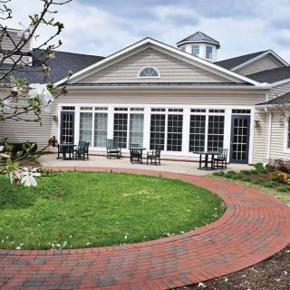 A beautifully designed house with a large window front and a curved brick pathway leading through a well-maintained lawn.