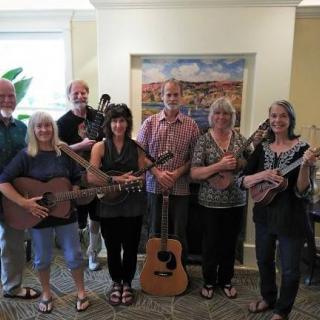 A group of musicians gathered indoors, each holding a string instrument.