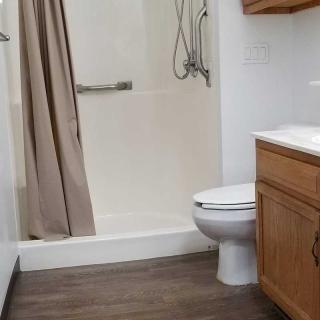 A compact modern bathroom featuring a shower with a curtain, a toilet, and a wooden cabinet with sink.