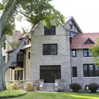 A large stone house with a red roof surrounded by greenery and trees.