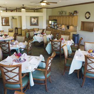 Bright dining room with neatly arranged tables and chairs, featuring a small kitchen area.