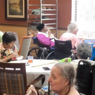 Elderly individuals in a nursing home dining area, some using wheelchairs.