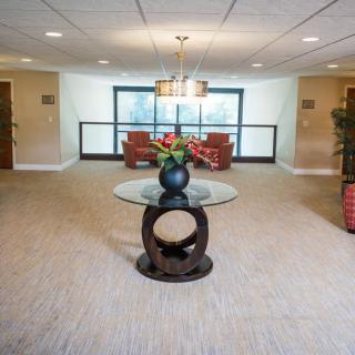 A well-decorated lobby with a central table and floral arrangement, surrounded by comfortable seating and large windows.