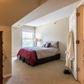A cozy bedroom with a neatly made bed, side lamp, and carpeted floor.