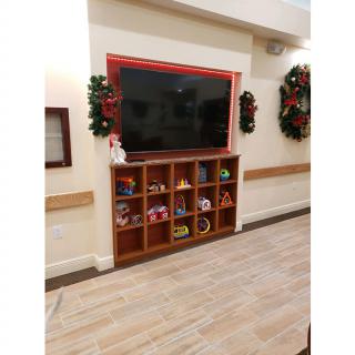 A TV mounted above shelves filled with toys, flanked by Christmas wreaths and decorations.