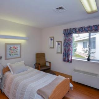 A simple, cozy hospital room with a single bed, chair, window, and wall art.