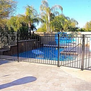A fenced outdoor pool area with palm trees and a sunny patio.