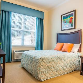 A cozy bedroom with a neatly made bed, vibrant pillows, and a window adorned with blue curtains.