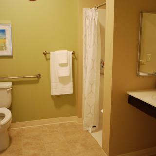 A spacious bathroom featuring a toilet, shower with curtain, sink, and towel rack.
