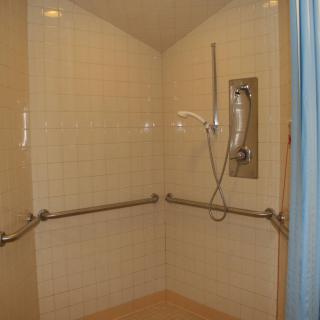 An accessible shower with grab bars and a handheld showerhead.