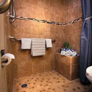 An accessible bathroom with tiled walls and floor, featuring a shower area, grab bars, and neatly arranged towels.