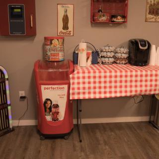 A cozy retro-themed corner featuring a red soda machine, checkered tablecloth, and vintage decor.