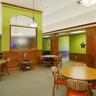 A cozy dining area with green walls, wooden accents, and several tables and chairs.