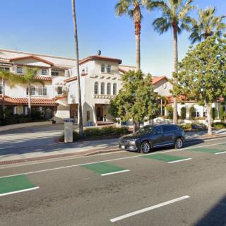 A sunny street view with palm trees, a car, and Spanish-style buildings.