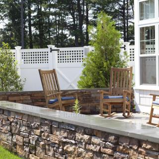 A serene outdoor patio area with wooden chairs, a stone wall, and greenery.