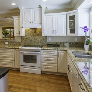 A modern kitchen with white cabinets, granite countertops, and wood flooring.