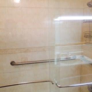A tiled bathroom shower with a grab bar and glass door.