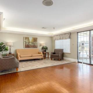 A cozy living room with wooden flooring, featuring a sofa, armchairs, and a coffee table, complemented by decorative plants and artwork.