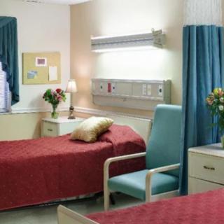 A clean and organized hospital room with red bedding and a comfortable chair.