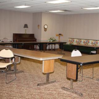 An empty meeting room with tables, chairs, and a piano.