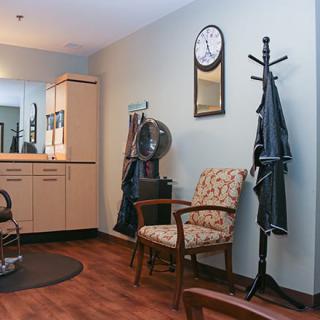 A cozy salon interior with a vintage-style chair, coat rack, and wall clock.